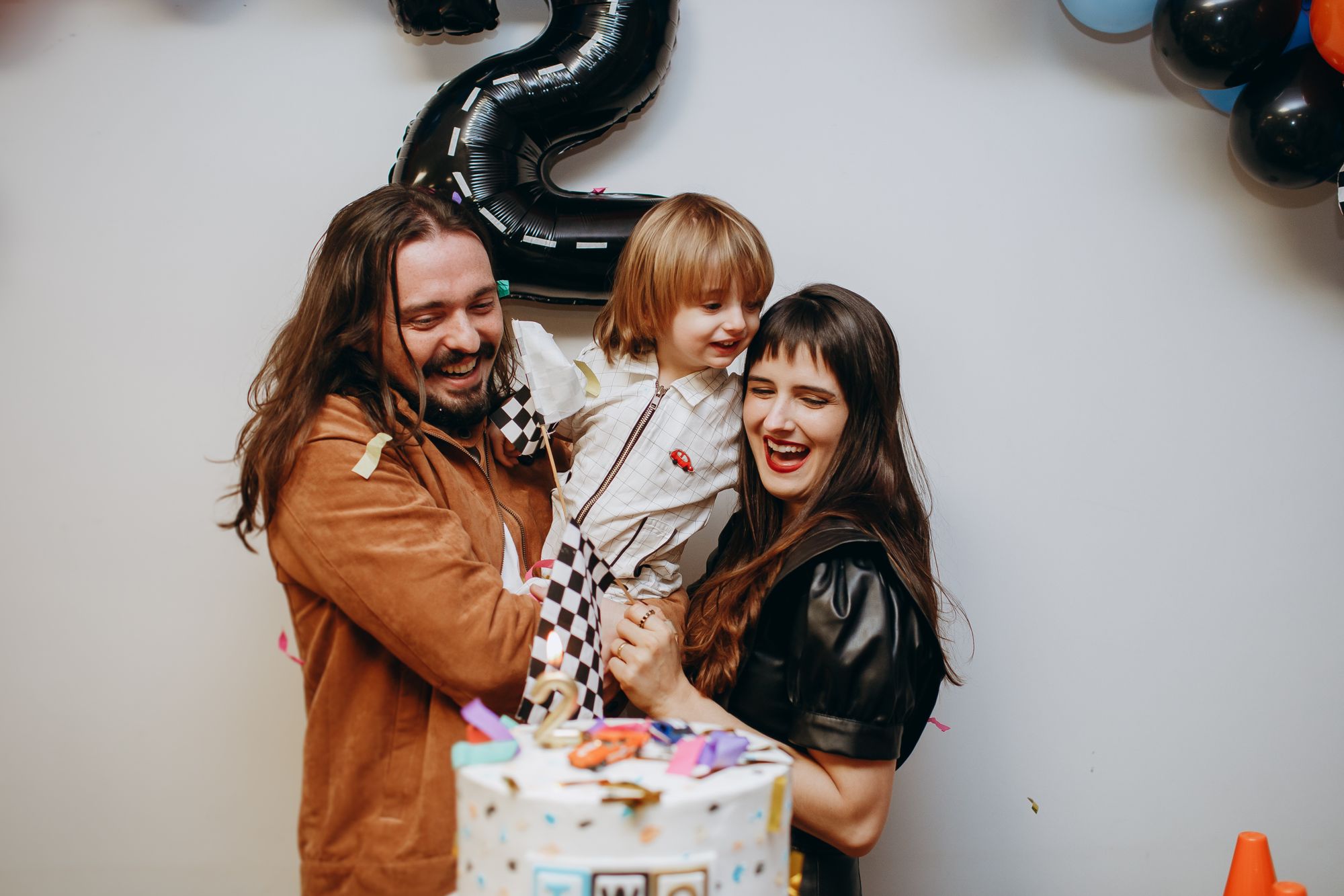 Parents laughing with their small child beside a birthday cake