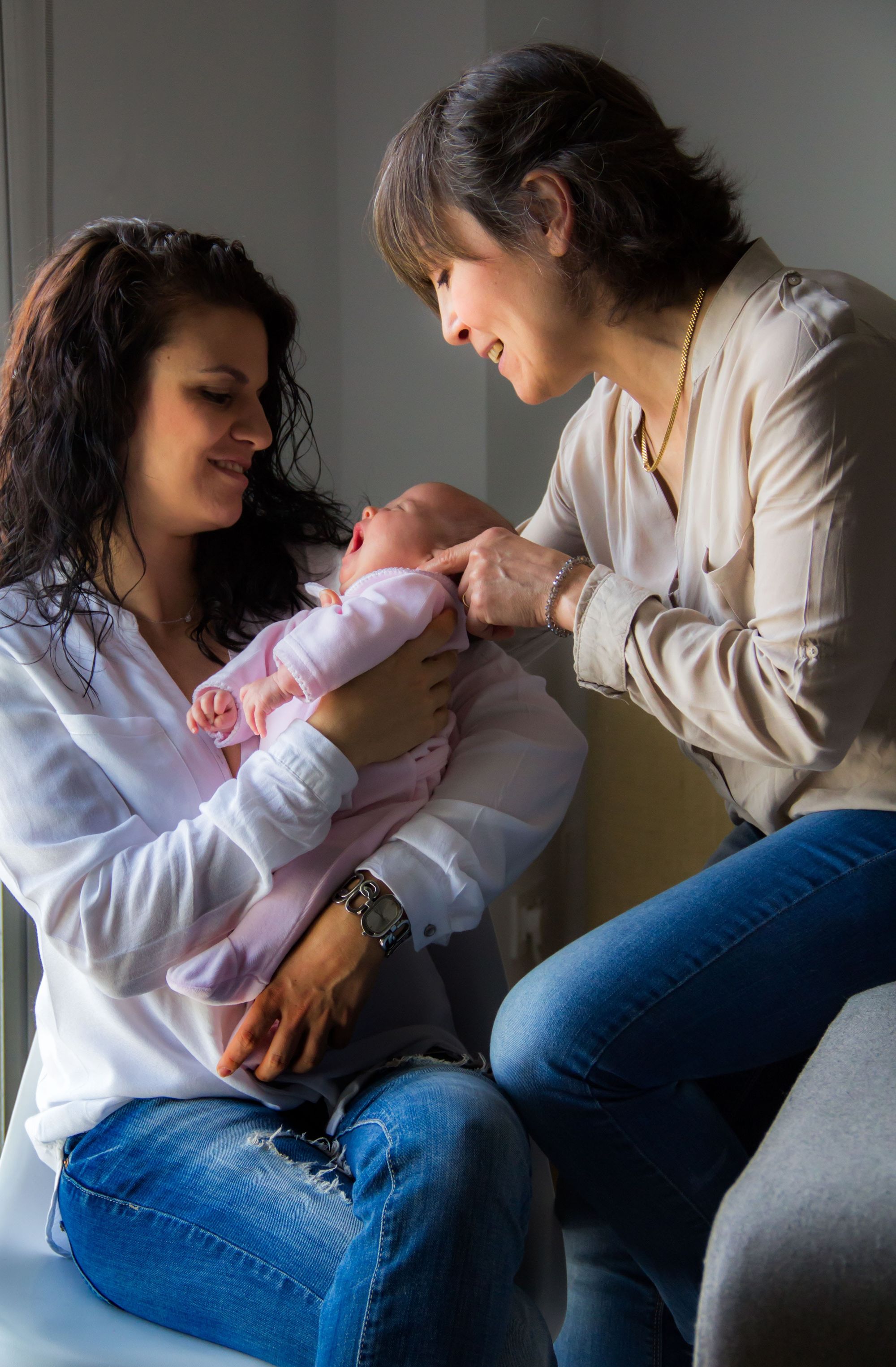 A new mother and grandmother smiling together over a newborn baby